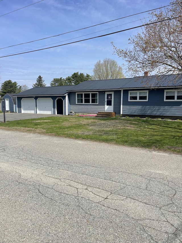 ranch-style home with an attached garage, a chimney, metal roof, aphalt driveway, and a front lawn