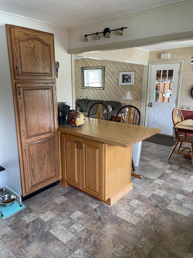 kitchen featuring a peninsula, brown cabinetry, a kitchen breakfast bar, stone finish floor, and wood walls