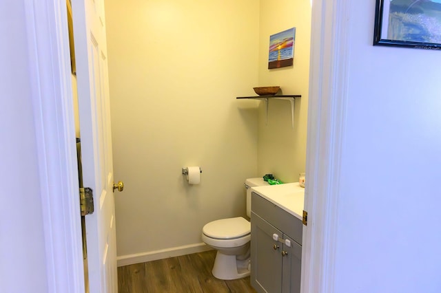 half bathroom featuring vanity, baseboards, toilet, and wood finished floors