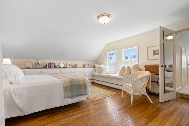 bedroom with a baseboard heating unit, vaulted ceiling, and hardwood / wood-style floors