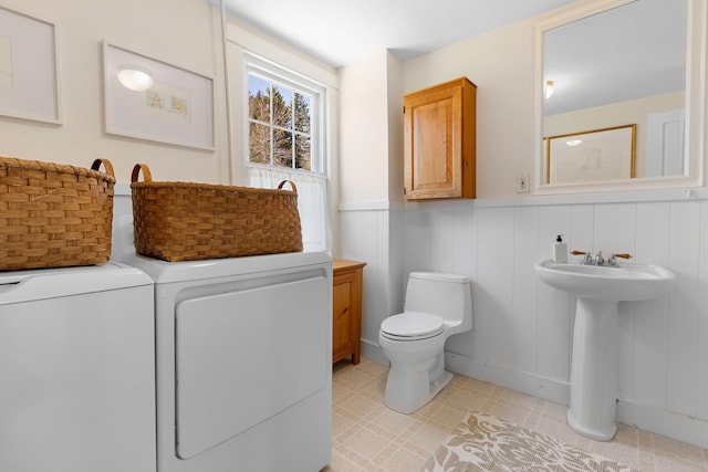 bathroom with wainscoting, toilet, tile patterned floors, washing machine and clothes dryer, and a sink