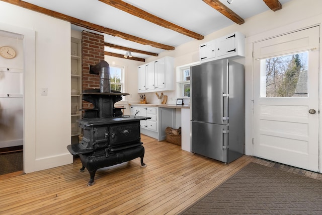 kitchen with freestanding refrigerator, a wood stove, beam ceiling, white cabinets, and light wood finished floors