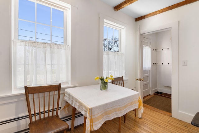 dining area with a baseboard radiator, light wood-style flooring, and beam ceiling