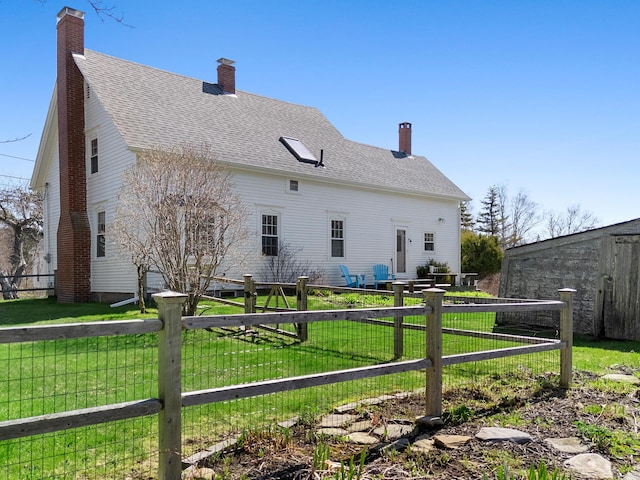 rear view of property with a lawn, a shingled roof, fence, and a chimney