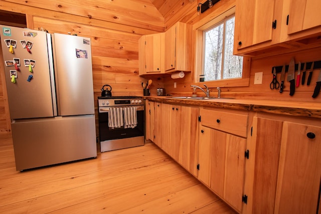 kitchen with wood walls, light brown cabinetry, a sink, light wood finished floors, and stainless steel appliances