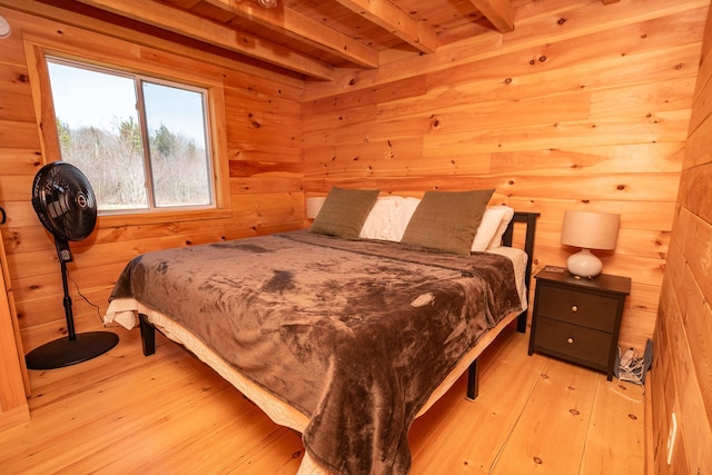 bedroom with wood walls, beam ceiling, and light wood-style flooring