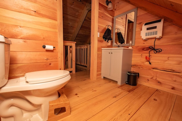bathroom featuring wood finished floors, vanity, lofted ceiling with beams, wooden walls, and heating unit