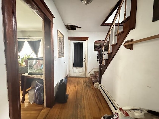 corridor with wood-type flooring, a baseboard radiator, and stairs