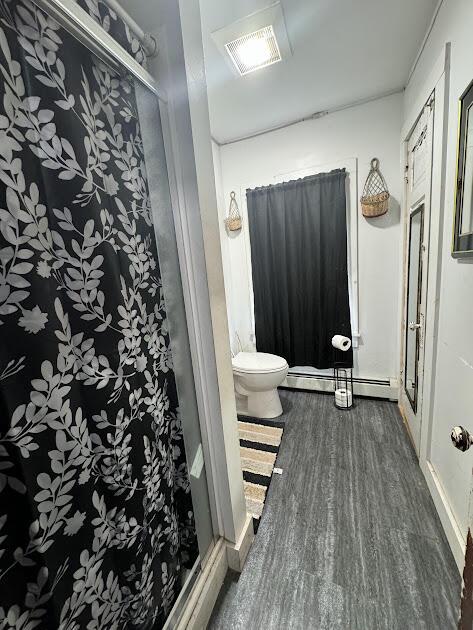 bathroom featuring visible vents, wood finished floors, toilet, walk in shower, and a baseboard radiator