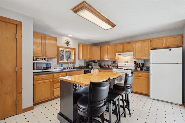 kitchen with white appliances, light floors, a breakfast bar area, under cabinet range hood, and a sink