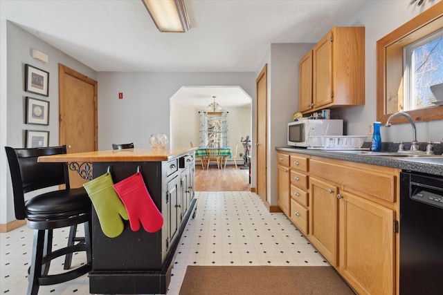 kitchen with light floors, black dishwasher, white microwave, a sink, and a notable chandelier