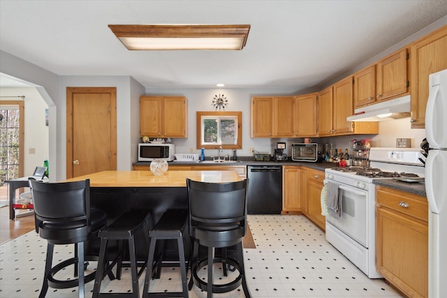 kitchen featuring a breakfast bar, white appliances, light floors, under cabinet range hood, and a sink