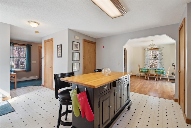 kitchen with butcher block countertops, a kitchen breakfast bar, a baseboard radiator, a chandelier, and arched walkways