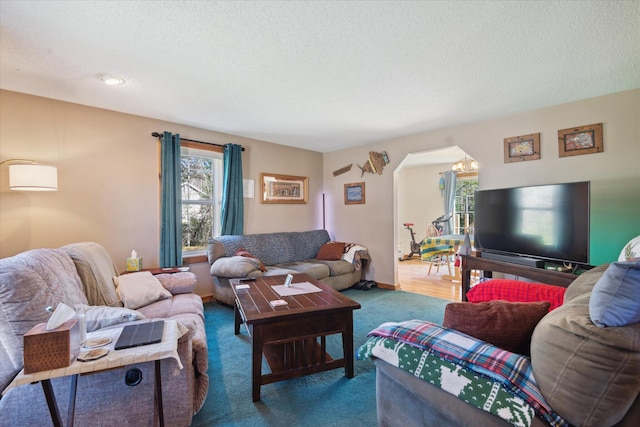 living area featuring arched walkways, a textured ceiling, a healthy amount of sunlight, and carpet flooring