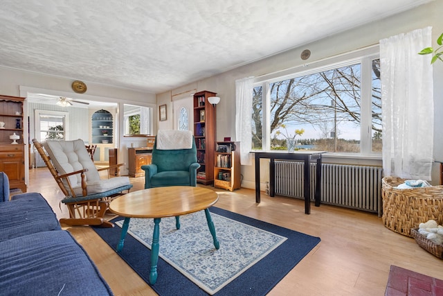 living area featuring wood finished floors, a textured ceiling, radiator heating unit, and a wealth of natural light