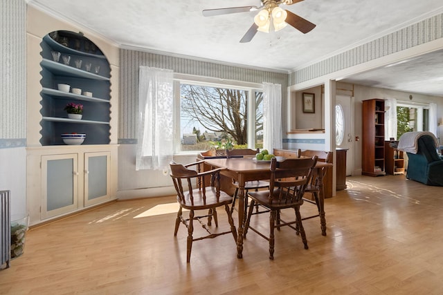 dining space featuring crown molding, a ceiling fan, wallpapered walls, and light wood-style flooring