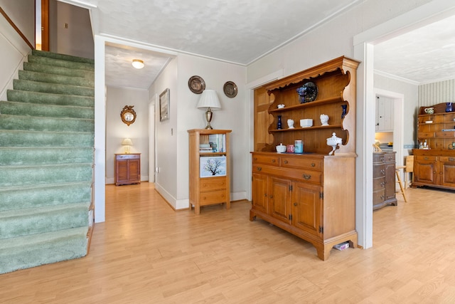 hall featuring light wood-type flooring, ornamental molding, stairs, and baseboards