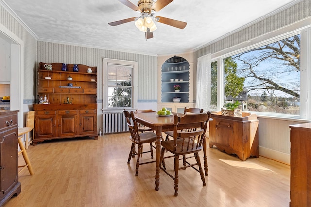 dining area featuring crown molding, light wood-style flooring, radiator, and wallpapered walls