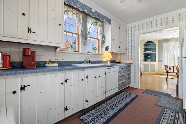 kitchen featuring crown molding, white dishwasher, white cabinets, a sink, and wallpapered walls