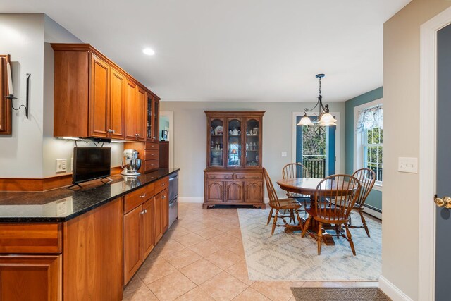 kitchen with dark stone countertops, brown cabinets, decorative light fixtures, light tile patterned flooring, and glass insert cabinets