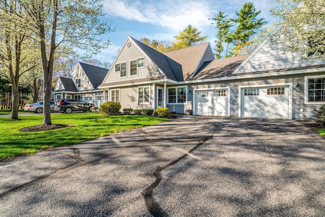 shingle-style home featuring an attached garage, a front lawn, and aphalt driveway