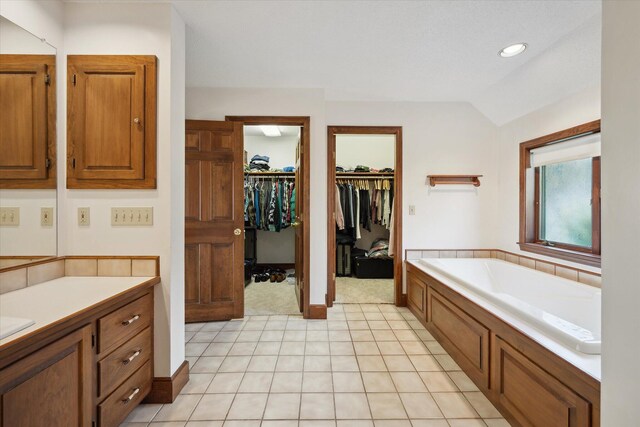 bathroom with a garden tub, vanity, lofted ceiling, a spacious closet, and tile patterned flooring