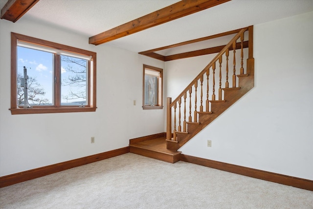 carpeted spare room featuring beamed ceiling, baseboards, and stairs