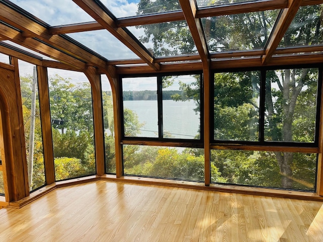 unfurnished sunroom with a water view, a skylight, wood finished floors, and healthy amount of natural light
