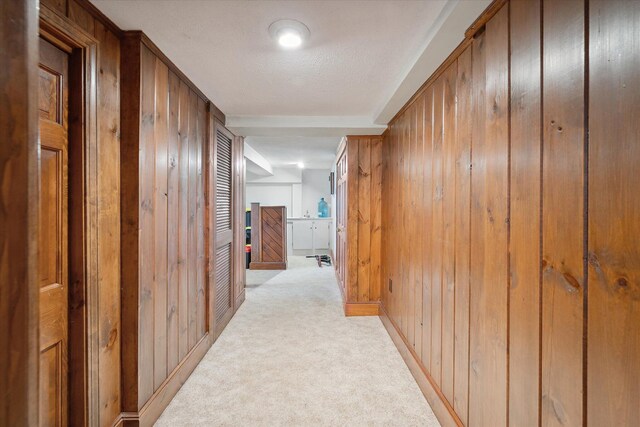 hall with wooden walls, light colored carpet, and baseboards