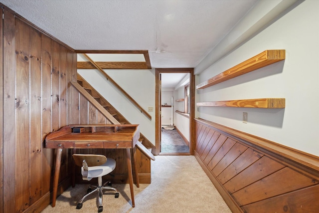 hall featuring light colored carpet, wood walls, a textured ceiling, and stairs