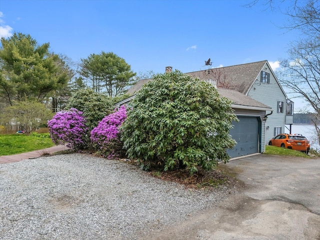 view of property exterior featuring asphalt driveway, a chimney, a shingled roof, and a garage
