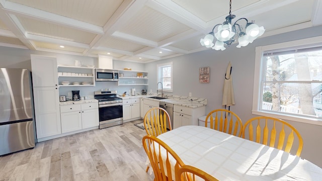 kitchen with appliances with stainless steel finishes, open shelves, a chandelier, light wood-style floors, and coffered ceiling