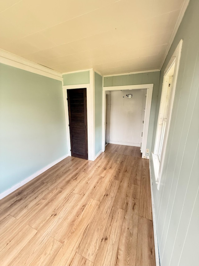 unfurnished bedroom featuring light wood-style floors, crown molding, and a closet