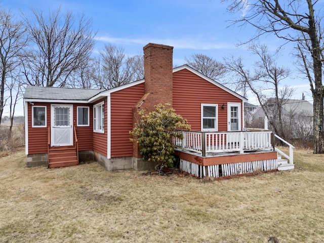 back of property featuring a wooden deck, roof with shingles, a chimney, entry steps, and a lawn