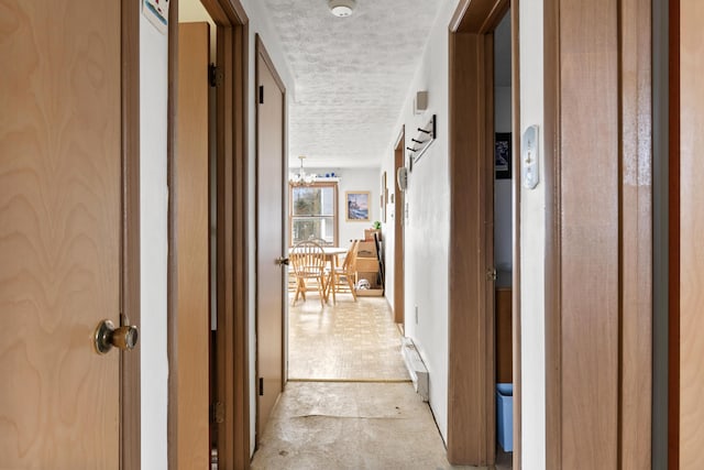 hall featuring a textured ceiling, an inviting chandelier, and light carpet