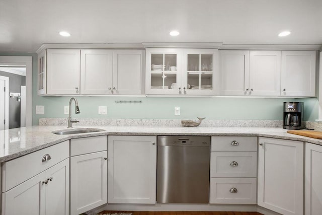 kitchen featuring light stone countertops, a sink, dishwasher, white cabinetry, and glass insert cabinets