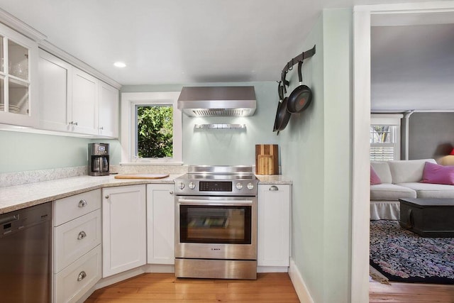 kitchen featuring wall chimney range hood, stainless steel appliances, white cabinetry, and light wood-style flooring