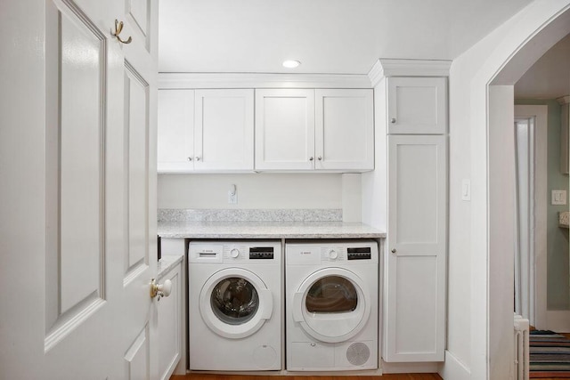 clothes washing area with washer and dryer, arched walkways, recessed lighting, and cabinet space