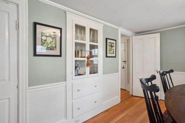 office space featuring light wood-type flooring, ornamental molding, and a wainscoted wall