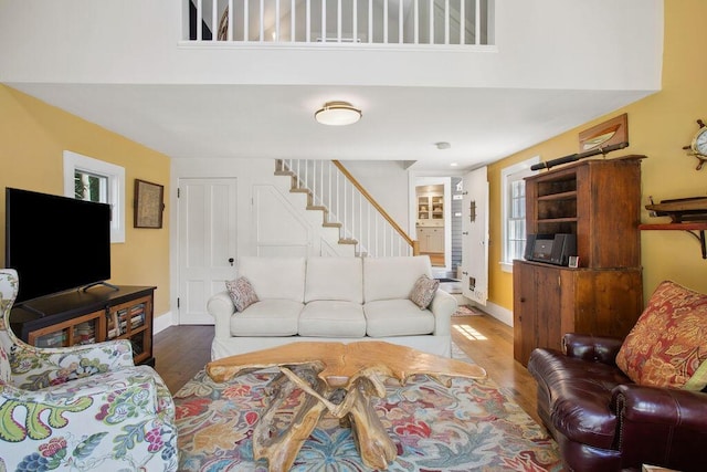 living area with baseboards, plenty of natural light, stairs, and wood finished floors