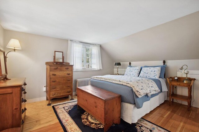 bedroom with radiator heating unit, lofted ceiling, and light wood-style floors