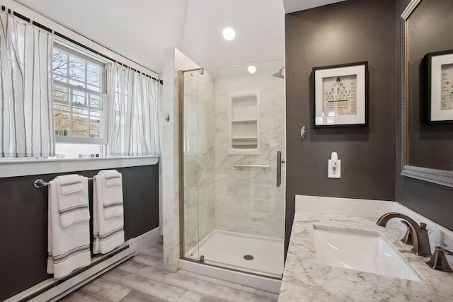full bathroom featuring a sink, a baseboard heating unit, wood finished floors, and a shower stall
