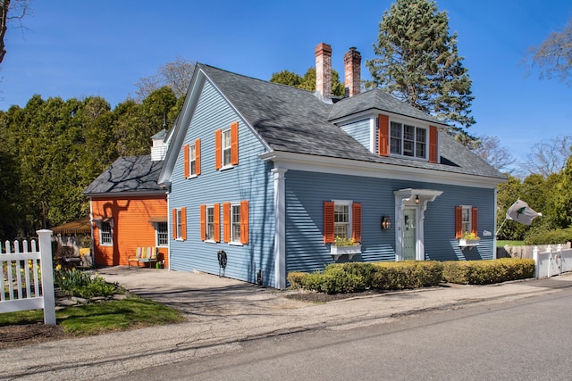 view of front of house with roof with shingles, fence, driveway, and a chimney