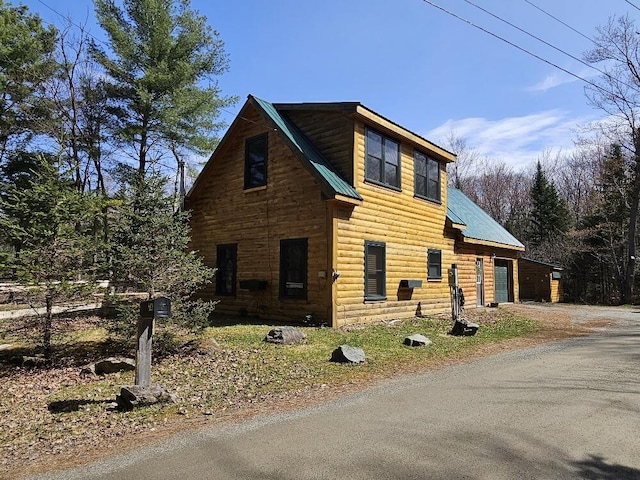 view of front of home featuring a garage, dirt driveway, faux log siding, and metal roof