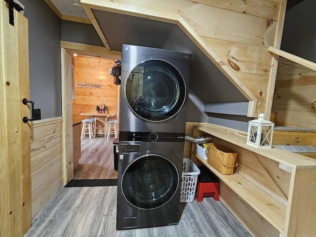 washroom with laundry area, stacked washer and dryer, wood finished floors, wooden walls, and a barn door