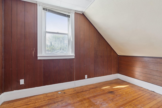 additional living space with wood finished floors, baseboards, lofted ceiling, and wooden walls