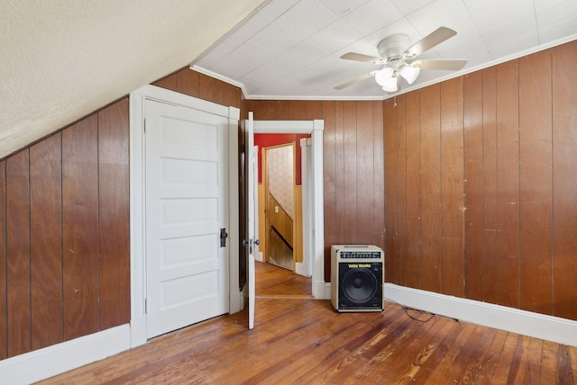 additional living space featuring heating unit, ceiling fan, wood finished floors, and wooden walls