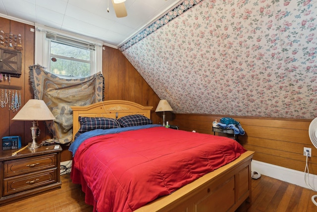 bedroom with wooden walls, a ceiling fan, lofted ceiling, and hardwood / wood-style floors