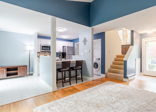 135 Portland Ave Unit 803, Old Orchard Beach, ME 04064 - kitchen with washer / dryer, stainless steel appliances, white cabinetry, a kitchen breakfast bar, and light wood-type flooring