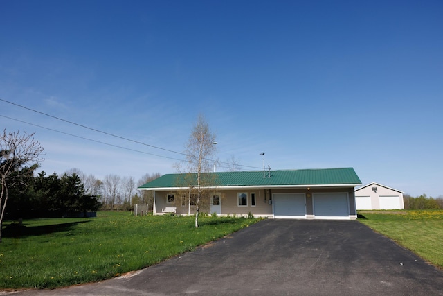 ranch-style home with an attached garage, a front yard, driveway, and metal roof